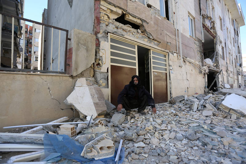 A man sits outside a damaged belonging following an earthquake in Sarpol-e Zahab county in Kermanshah