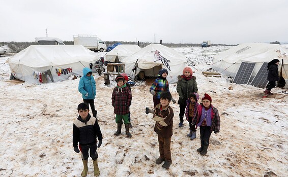 Internally displaced children stand on snow near tents at a makeshift camp in Azaz