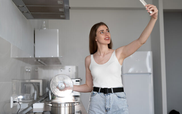 Young woman standing by the stove in the kitchen. removes a recipe for cooking.