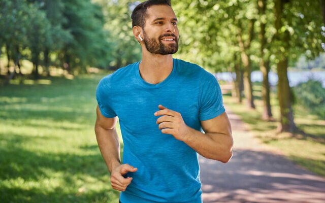 Happy man running in the park listening to music on headphones on a summer sunny day